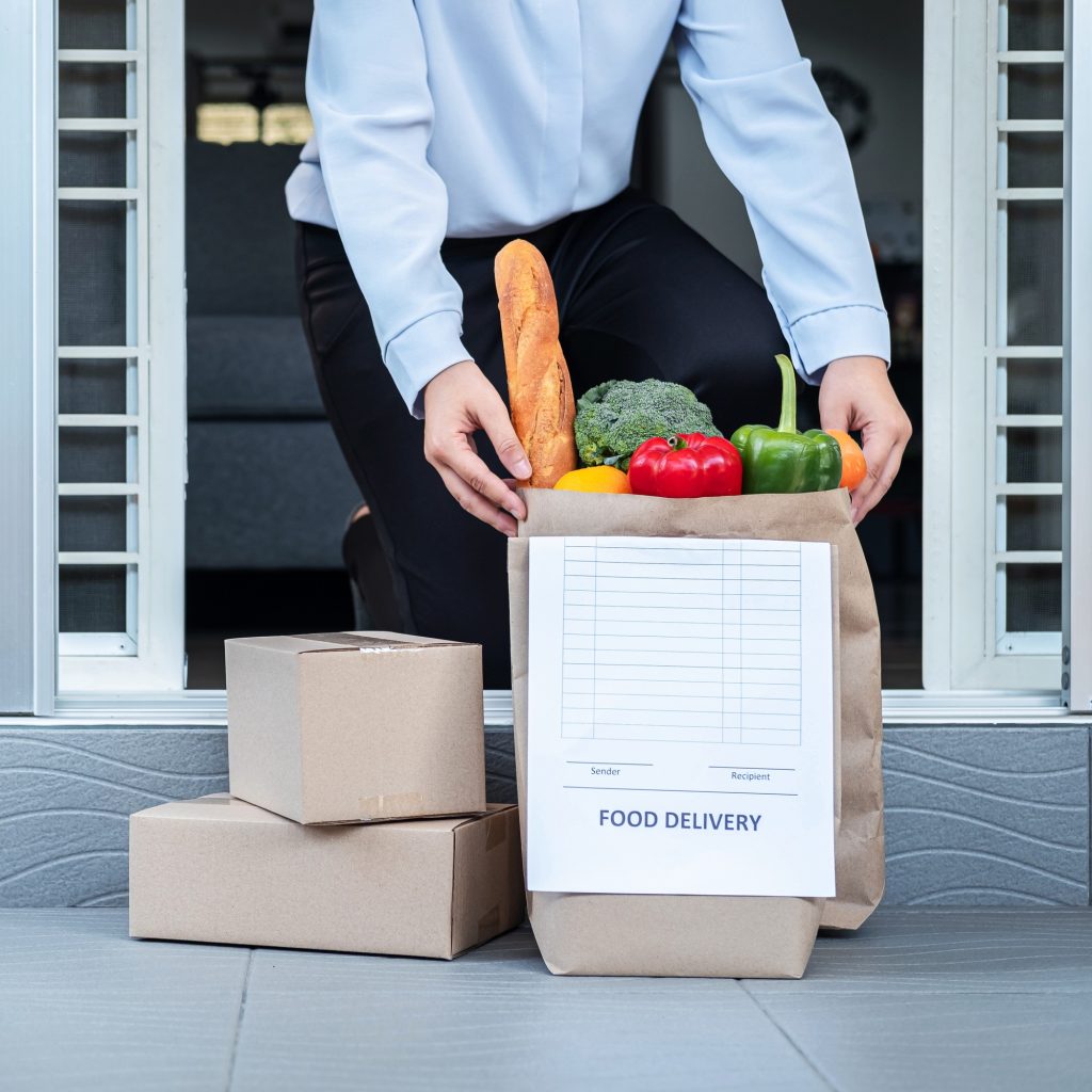 Asian woman customer in quarantine time order food delivery online and courier place grocery bag